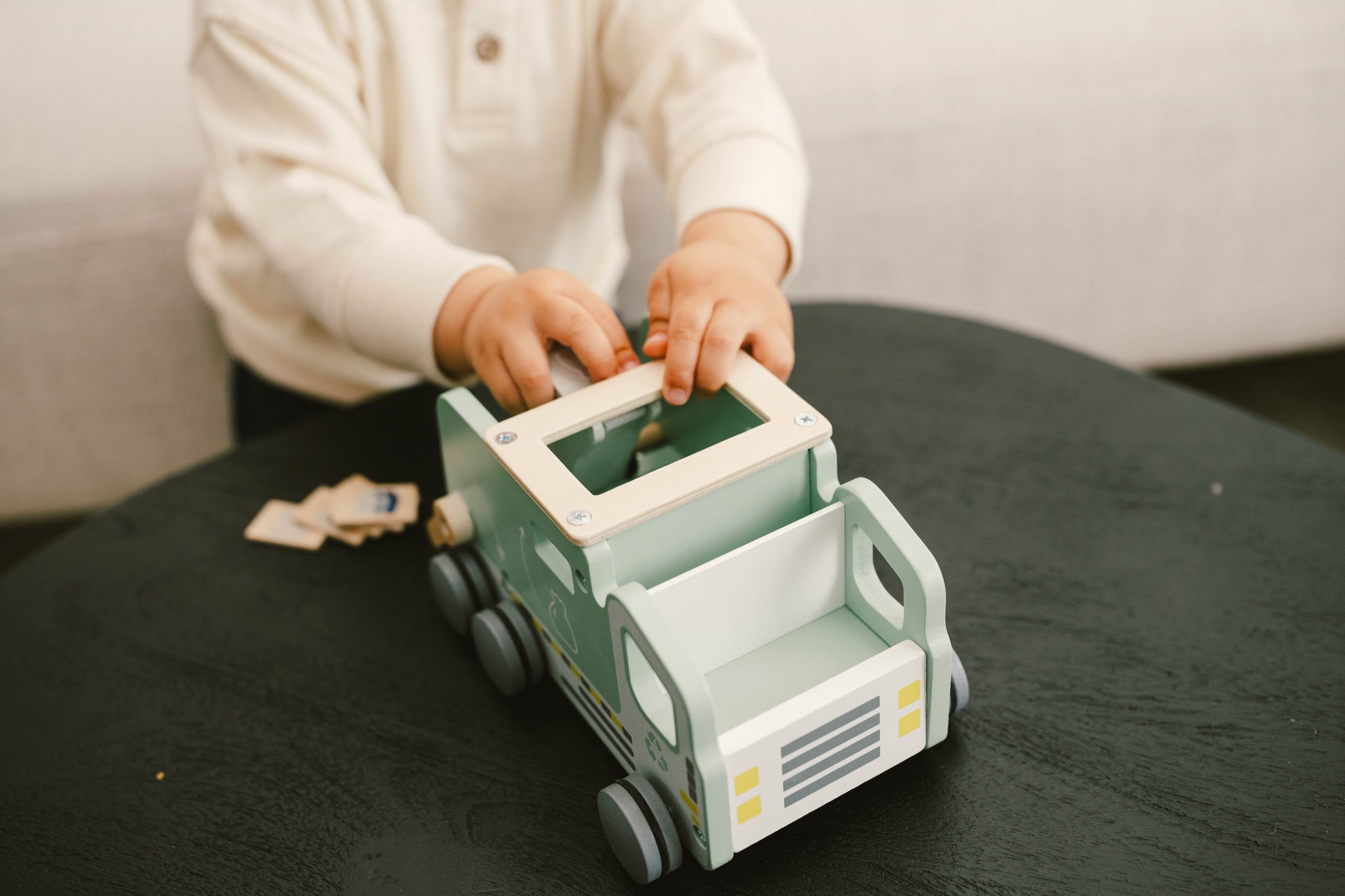 A wooden recycling truck toy with green accents and recycling symbols, alongside two recycling bins and sorting tiles.