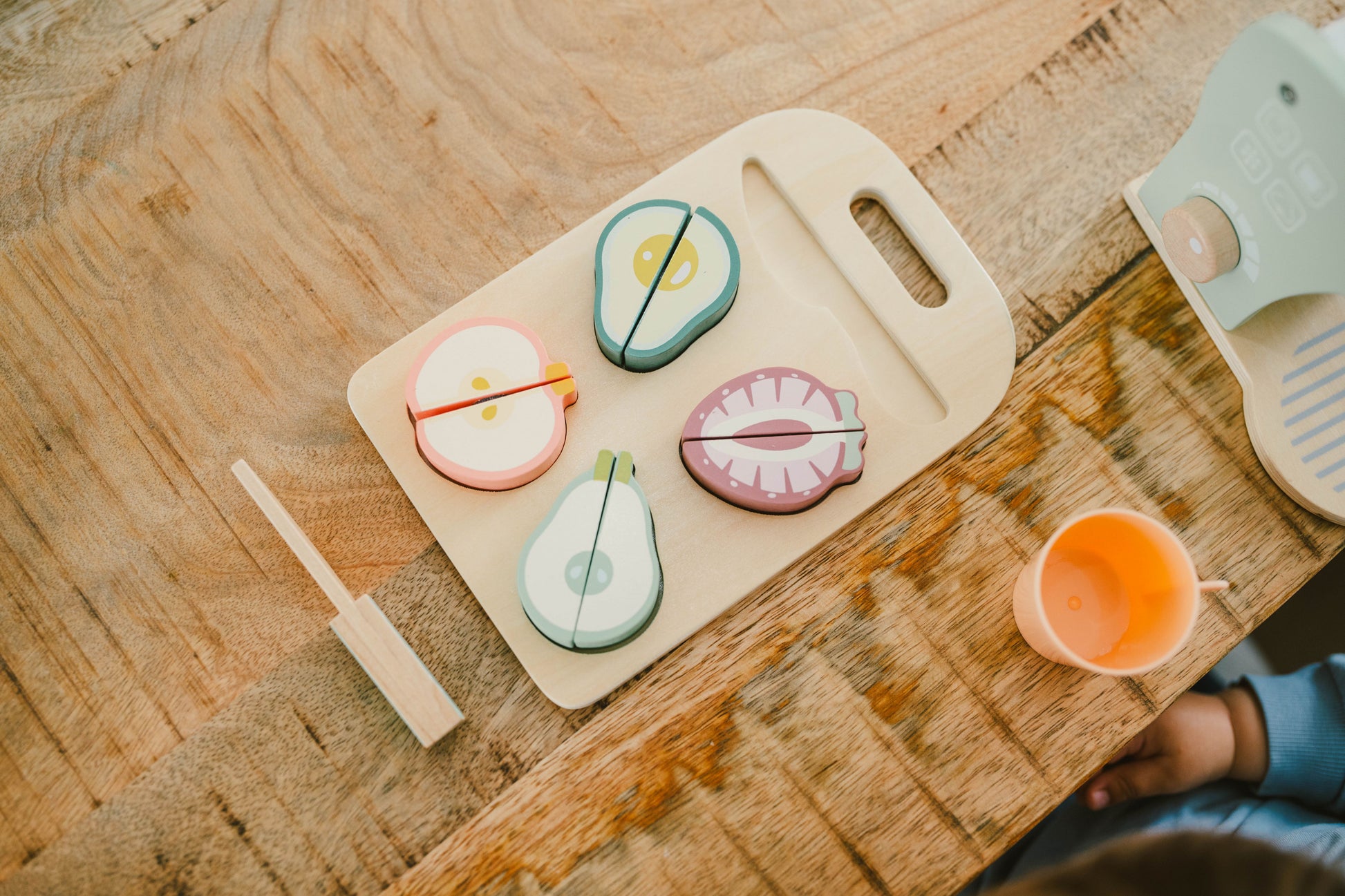 A wooden cutting board with colorful, realistic-looking fruit pieces arranged on top of it, and a wooden knife beside them.