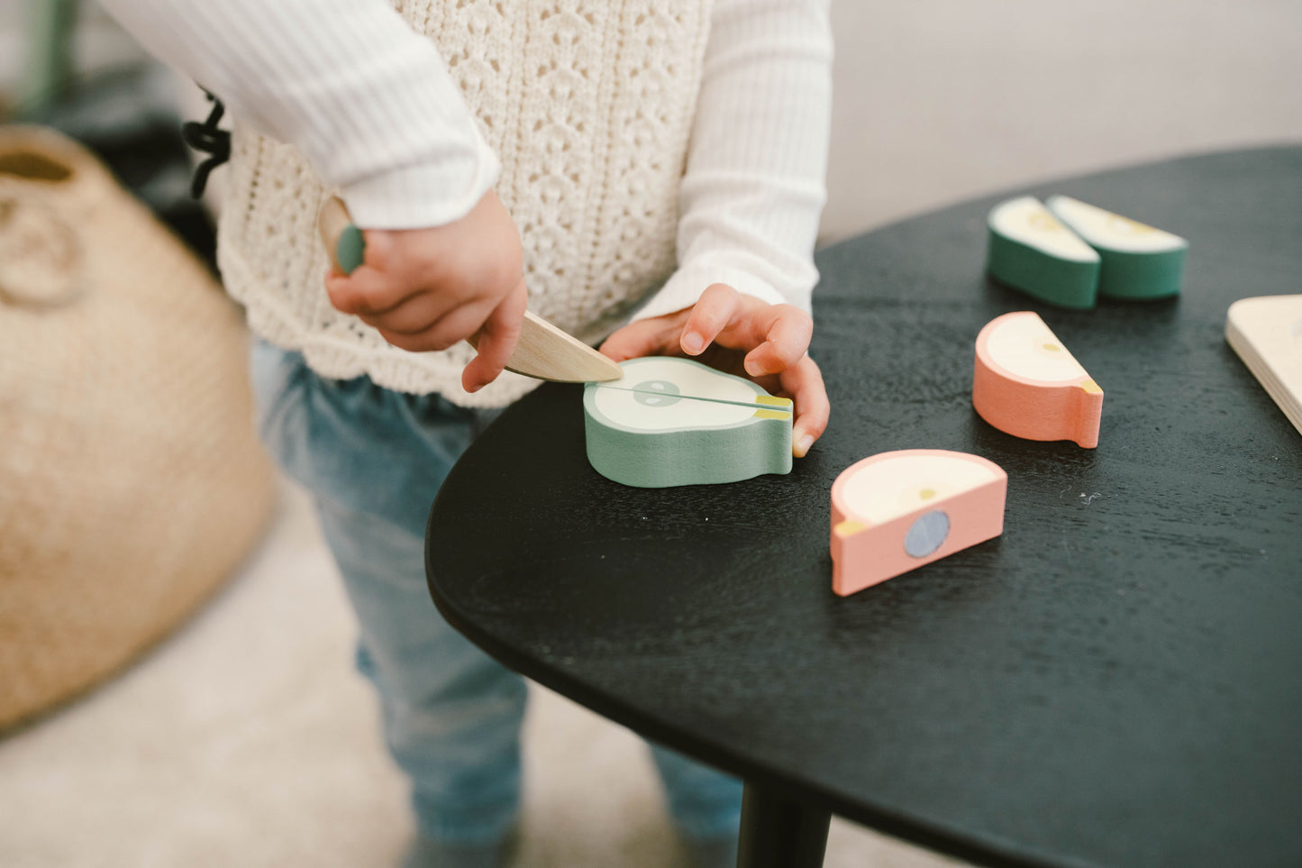 Girl playing with wooden fruits, cutting them with a wooden knife