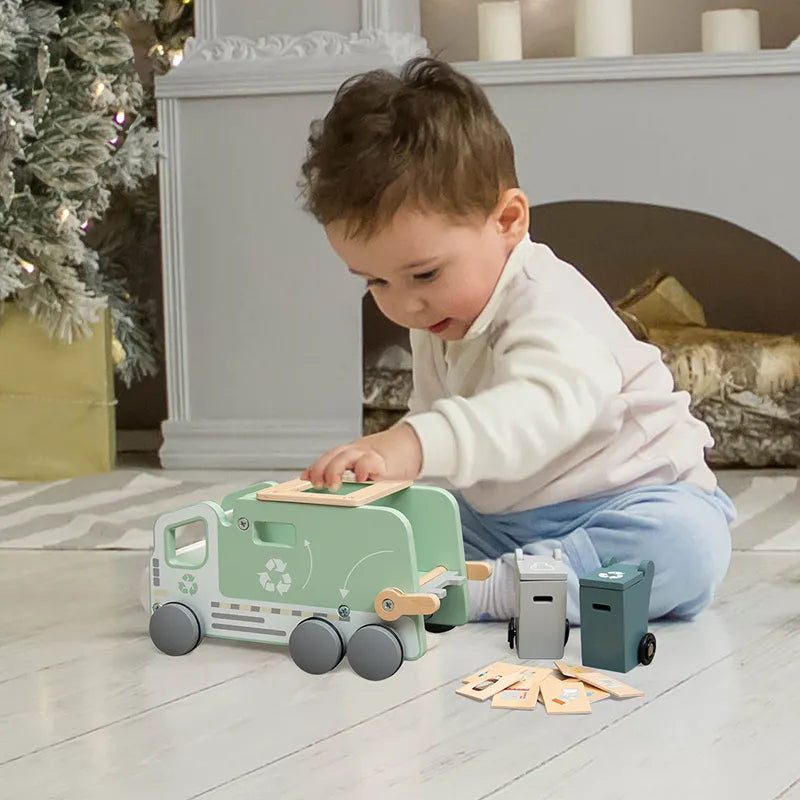Boy playing with a wooden recycling truck toy with green accents and recycling symbols, alongside two recycling bins and sorting tiles.