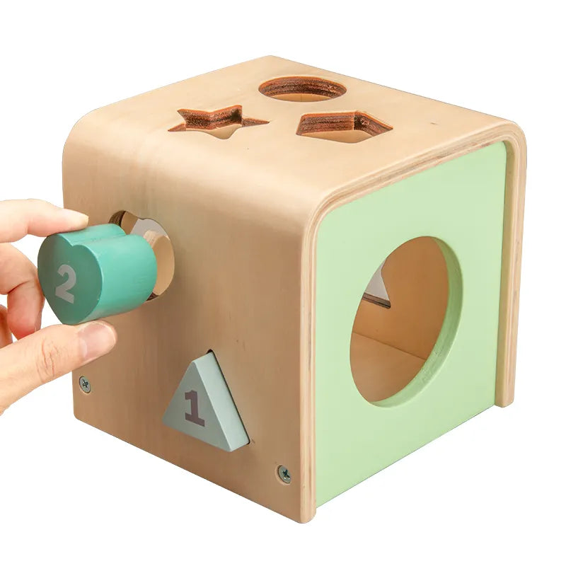 A wooden shape sorting cube with various holes for shapes, and colorful numbered shapes being inserted by a hand.