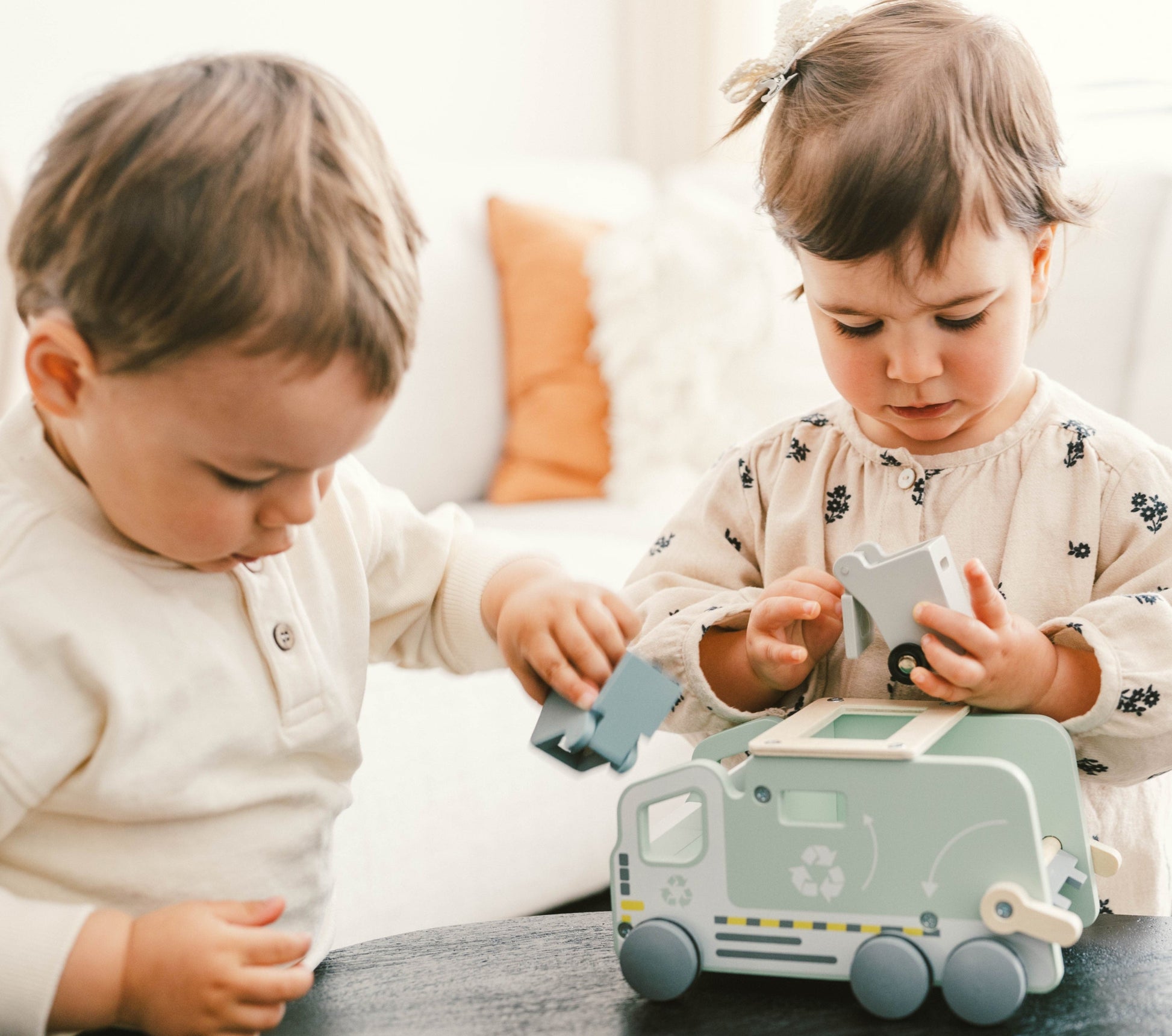 Two children playing with a recycling toy truck on a table.